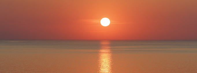 Incredible beautiful golden sunset over the Baltic sea. Sun disc hanging over the horizon line. The sea is calm and peaceful during this magic sunny summer sunset time