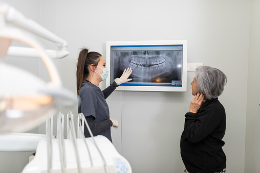 Dentist shows an X-ray of the mouth to an older woman in her 70s on the screen