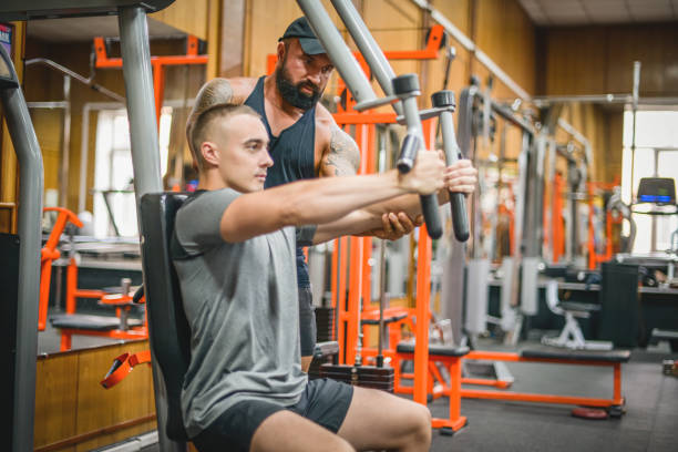 istock Man doing exercises in the gym with a man trainer athletic physique 1421088913