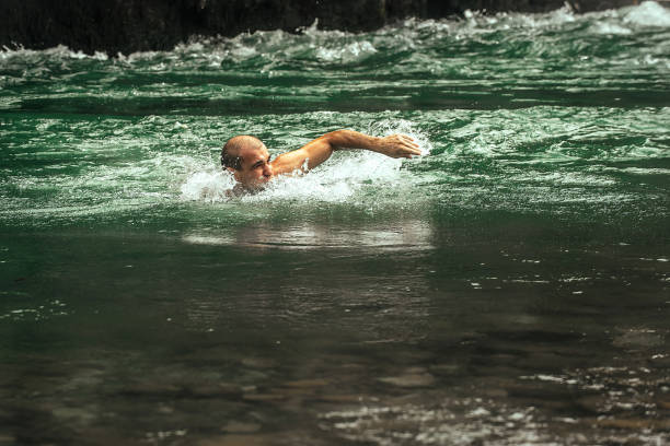 a man actively swims in a cold mountain river with a rapid current on a sunny day. Active sports tourism