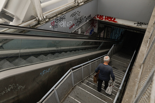 Bucharest, Romania - September 3, 2022: Senior man walks down a dark, dirty and vandalised stairway in Bucharest.