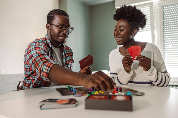 Young people enjoying at home and playing board game African-American young people sitting at the table in the living room and having fun while playing a board game friends playing cards stock pictures, royalty-free photos & images