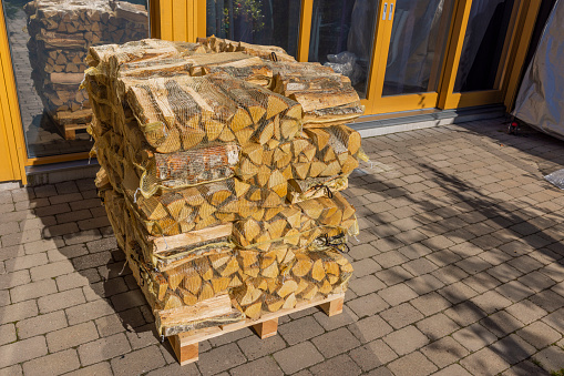 Close up view of birch firewood in transport nets on pallet in front of exterior facade of modern villa. Sweden.