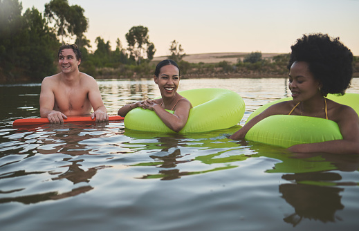 Fun group of diverse friends relaxing in lake water, enjoying nature and bonding on a getaway vacation in the countryside together. Happy men and women laughing, smile and looking relaxed on holiday