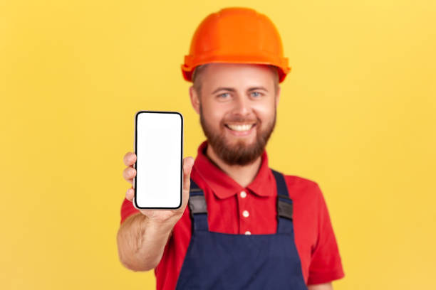 istock Builder man in uniform and protective helmet holding smart phone with blank screen for advertisement 1421097677