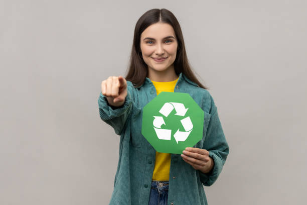 istock Optimistic woman holding recycling sign pointing finger at camera, worrying about environment. 1421098062
