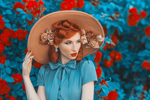 Awesome redhead model expresses emotions. Valentines Day background. Fabulous retro girl with red lips in mint dress on awesome summer background. Woman portrait. Roses bush.