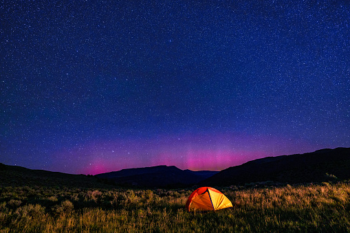 Glowing Tent with Stars Around Polaris North Star - Camping in beautiful dark sky mountain area with crisp stars centered around Polaris in Ursa Minor constellation. Northern Lights Aurora Borealis glowing in sky.