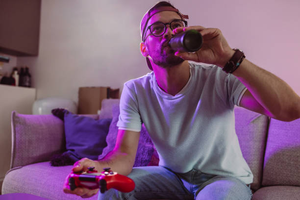 young man drinking beer at home while playing video game - after work beautiful people beer beer bottle imagens e fotografias de stock