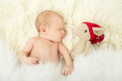 cute newborn girl with mouse toy sleeping on white fur