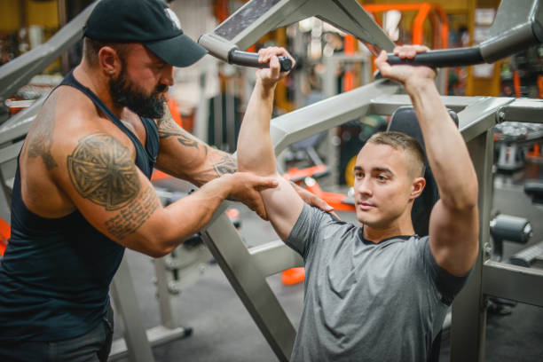 istock Man doing exercises in the gym with a man trainer athletic physique 1421107691