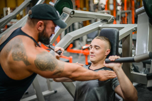 istock Man doing exercises in the gym with a man trainer athletic physique 1421108249