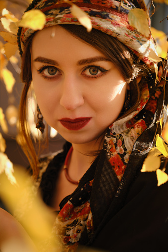 young gypsy woman in autumn yellow leaves, looking at camera