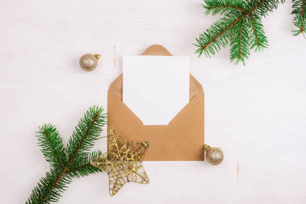 istock Open brown envelope with blank white card and Christmas decorations on white wooden table. Top view, flat lay, mockup 1421109407