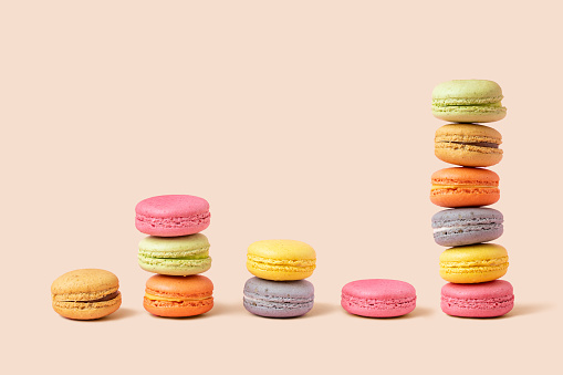 Stack and diagram of macaroons as coins, forming a financial graph on beige background. Metaphors and concept
