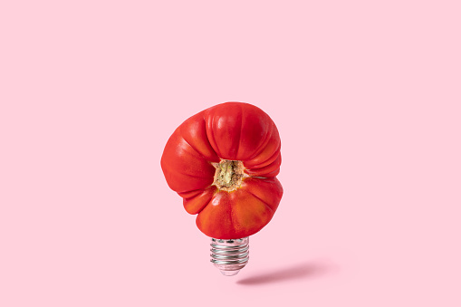 An alternative lamp. Idea and sour emotions. Red tomato as a light source on pink background. Contemporary art still life, Metaphors