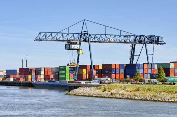 Rotterdam, Netherlands - August 2022: Large mobile crane lifting a shipping containers from an industrial barge on the river near Rotterdam