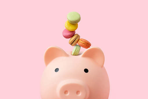 Macaroons as money coins in a pink piggy bank on a beige background. Objects as Metaphors concept.