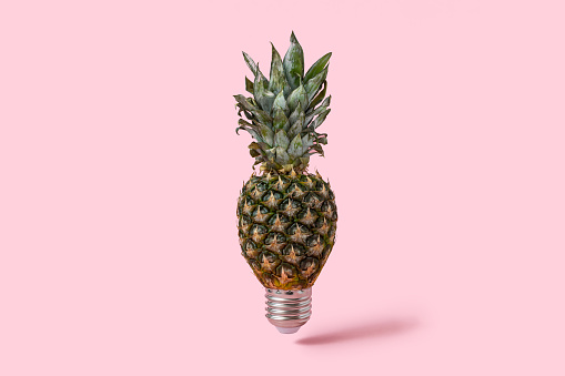 An alternative lamp. Idea and sour emotions. Pineapple as a light source on pink background. Contemporary art still life, Metaphors