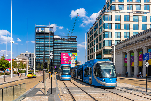 Birmingham United Kingdom Two blue trams passing on the street with people near the vehicle and on the street