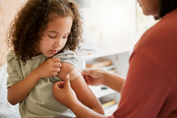 Photo of Covid nurse vaccinating child putting a bandage on at a clinic. Doctor applying plaster on girl after an injection at health centre. Pediatric, immunity and prevention at medical children's hospital