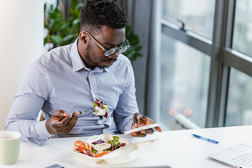 A young man is using his lunch break for eating and surfing the web on a mobile phone.