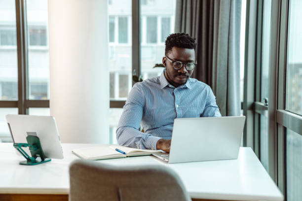 Young businessman working at his office Portrait of African-American businessman using a laptop at the office. He is concentrating on his work black man laptop stock pictures, royalty-free photos & images