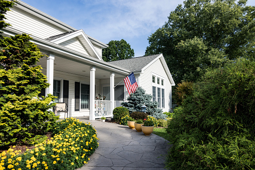 Yellow marigolds flower bed in late summer morning full bloom lines the curved concrete front walkway of a suburban residential district neighborhood colonial style home near Rochester, New York State, USA in early September.