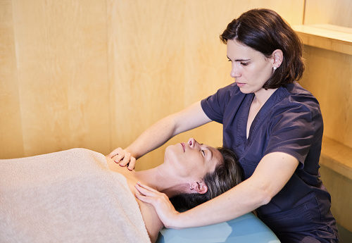 Physiotherapist giving a shoulder massage to a mature middle-aged woman. They are in a spa.