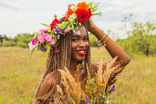 Beautiful african woman in flower wreath and dress on background of nature. Authentic style. Stylish accessories. Beauty portrait. Earrings and necklace. Fashion style