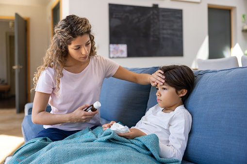 Mother at home checking if her sick son has fever by touching his forehead - healthcare and medicine concepts