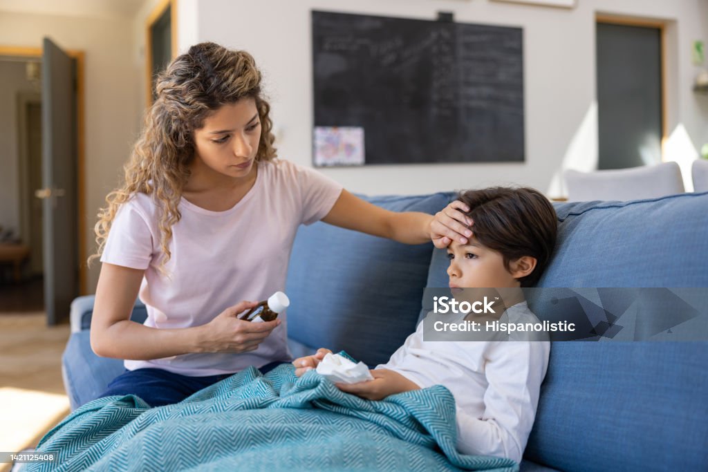 Mother at home checking if her sick son has fever Mother at home checking if her sick son has fever by touching his forehead - healthcare and medicine concepts Fever Stock Photo