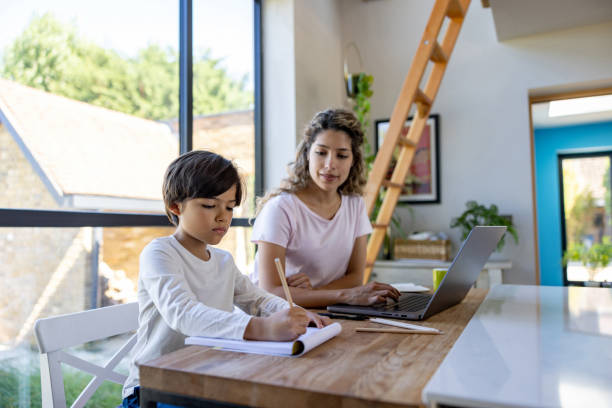 istock School boy doing his homework while his mother is working at home 1421125530