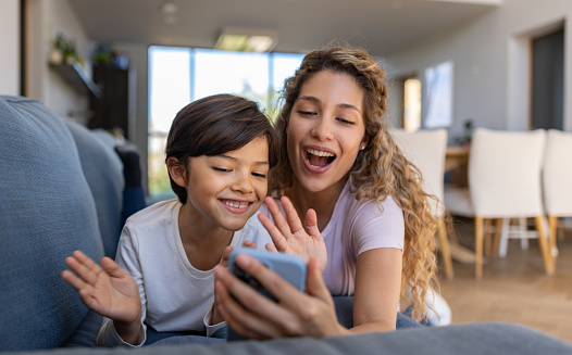 Happy Latin American mother and son at home greeting on a video call - telecommunications concepts