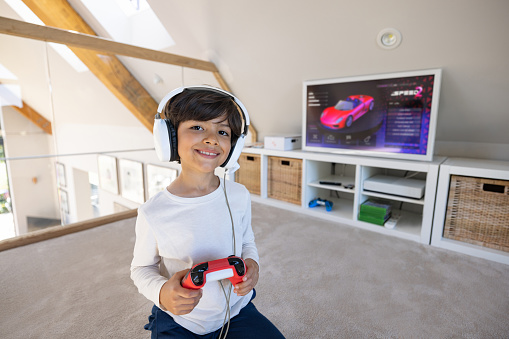 Portrait of a happy boy playing video games at home using headphones and looking at the camera smiling- lifestyle concepts