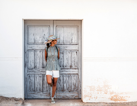 A woman wearing a hat and white shorts, leaning against a wooden door and looking to the side. concept rest after a walk.