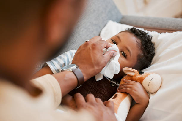 kranker, kranker und kranker kleiner junge, der an erkältung, grippe oder covid leidet und zu hause auf dem sofa liegt, während er sich mit papa die nase putzt. süßer sohn mit laufender nase und im wohnzimmer von oben ruhend - krankheit stock-fotos und bilder