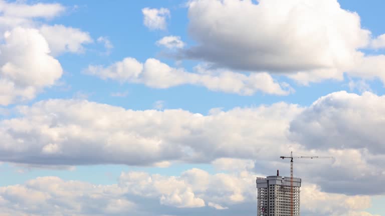 BUILDING CONSTRUCTION. Isolated. With a working crane on the roof of a skyscraper. Construction of a modern high-rise building using modern technologies. Lots of clear sky with clouds. Time-lapse.