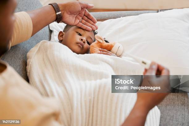Sick Flu And Cold Child In Bed Sad And Ill With Allergy And Unwell At Home With His Worried Mother Parents Hand On Sons Forehead For His Temperature As She Checks His Fever With A Thermometer Stock Photo - Download Image Now