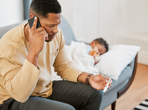 Worried, concerned and serious father talking on phone call, caring for sick son and taking temperature check on couch at home. Parent consulting with professional and taking care of son with fever