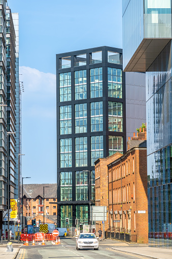 Manchester United Kingdom city street with a modern tower and some historic red brick fascades. A car with people can be seen in the foreground