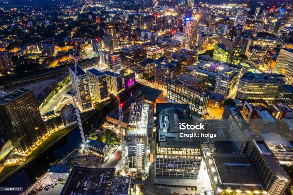 Manchester United Kingdom aerial shot of modern buildings with lots of counstruction in the central area of the city with historic canals and railways in the foreground by night Manchester - England Stock Photo