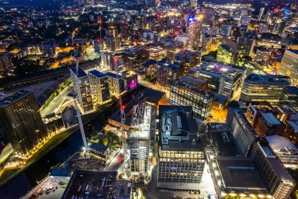 Manchester United Kingdom aerial shot of modern buildings with lots of counstruction in the central area of the city with historic canals and railways in the foreground by night
