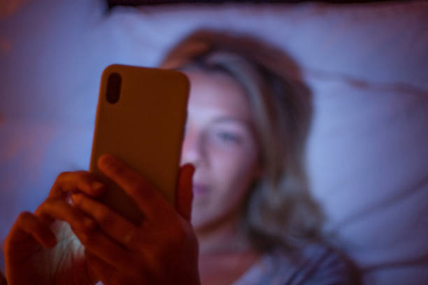 Defocussed image of Woman looking at a mobile phone in bed at night. stock photo