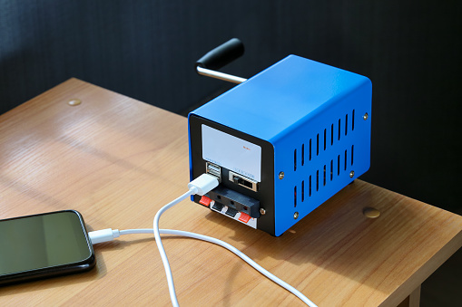 Portable electricity generator, rotate with your hand, USB cable is connected to smartphone for emergency situation, on table close-up