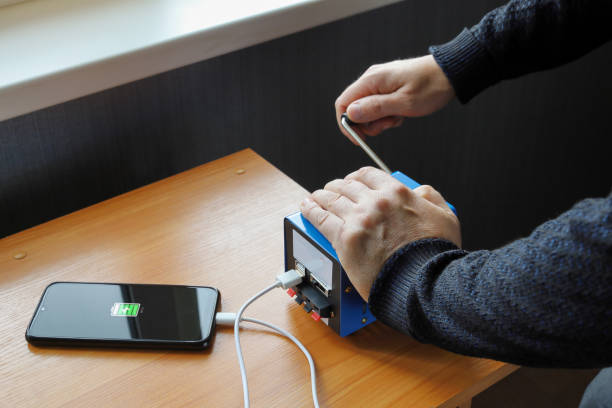 istock Human hands rotate handle of electricity generator, charge smartphone 1421132949