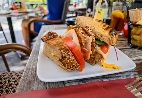 Front view of a clubsandwich with Chicken, egg salad, cheddar, bacon, tomato, served with sauce and nacho chips on a restaurant table. There are no trademarks and people in the shot.