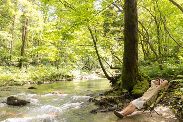 An outdoors man taking a nap or relaxing in a camping chair by a pristine mountain stream in the wilderness.