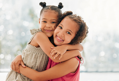 Cute, adorable and sweet young girls bond and hug with a happy and healthy childhood growing at home. Portrait of innocent and loving sisters with a bright smile, affection and relaxing in the house
