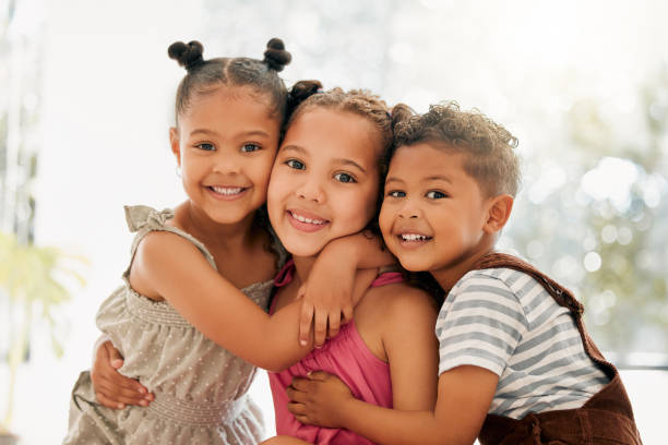 fratelli, ragazzi e bambine che si abbracciano e si legano insieme come una simpatica famiglia felice in casa durante l'estate. ritratto di bambini piccoli, fratelli e sorelle che sorridono, abbracciano e si godono la loro infanzia - sibling baby three people baby girls foto e immagini stock